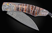Custom folding knife with a Damascus blade, engraved bolsters featuring Native American themes, and a striped brown and blue handle.