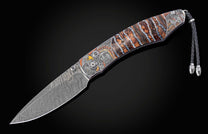 Folding knife with a patterned Damascus blade, engraved handle featuring an Indigenous chief, eagle, and wolf, brown and blue petrified wood inlays, and a braided leather lanyard.