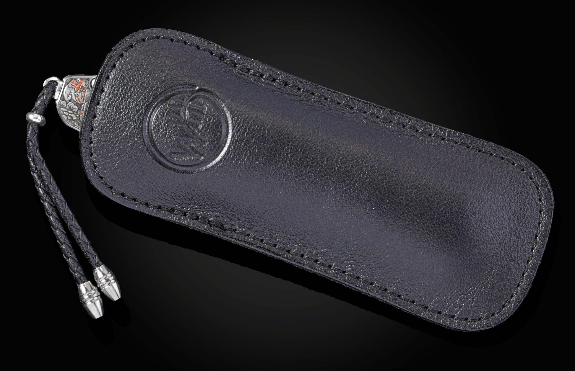 B12 Frontier Tales knife in a black leather sheath, featuring an embossed logo, braided lanyard, and silver-toned accents.