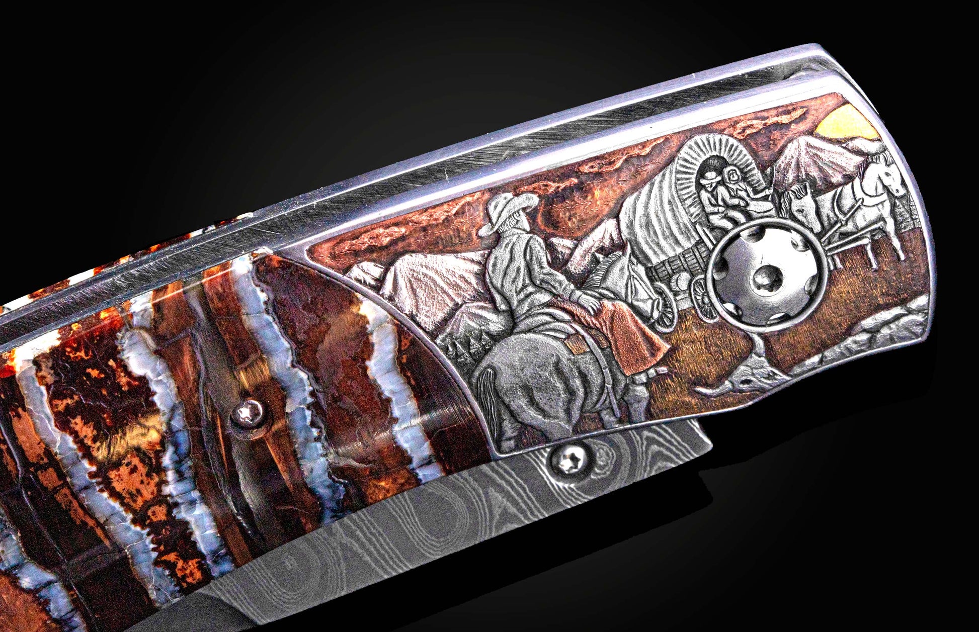 Folding knife with an engraved western frontier scene of a cowboy and covered wagon, alongside a layered brown and blue stone handle and Damascus blade.