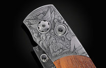 Close-up of an engraved metal folding knife featuring the Declaration of Independence signing scene, with circular hardware and a wood handle.