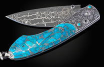 A folding knife with a stainless Damascus steel blade and a bright blue Kingman turquoise handle featuring silver engraving and gemstone inlays.