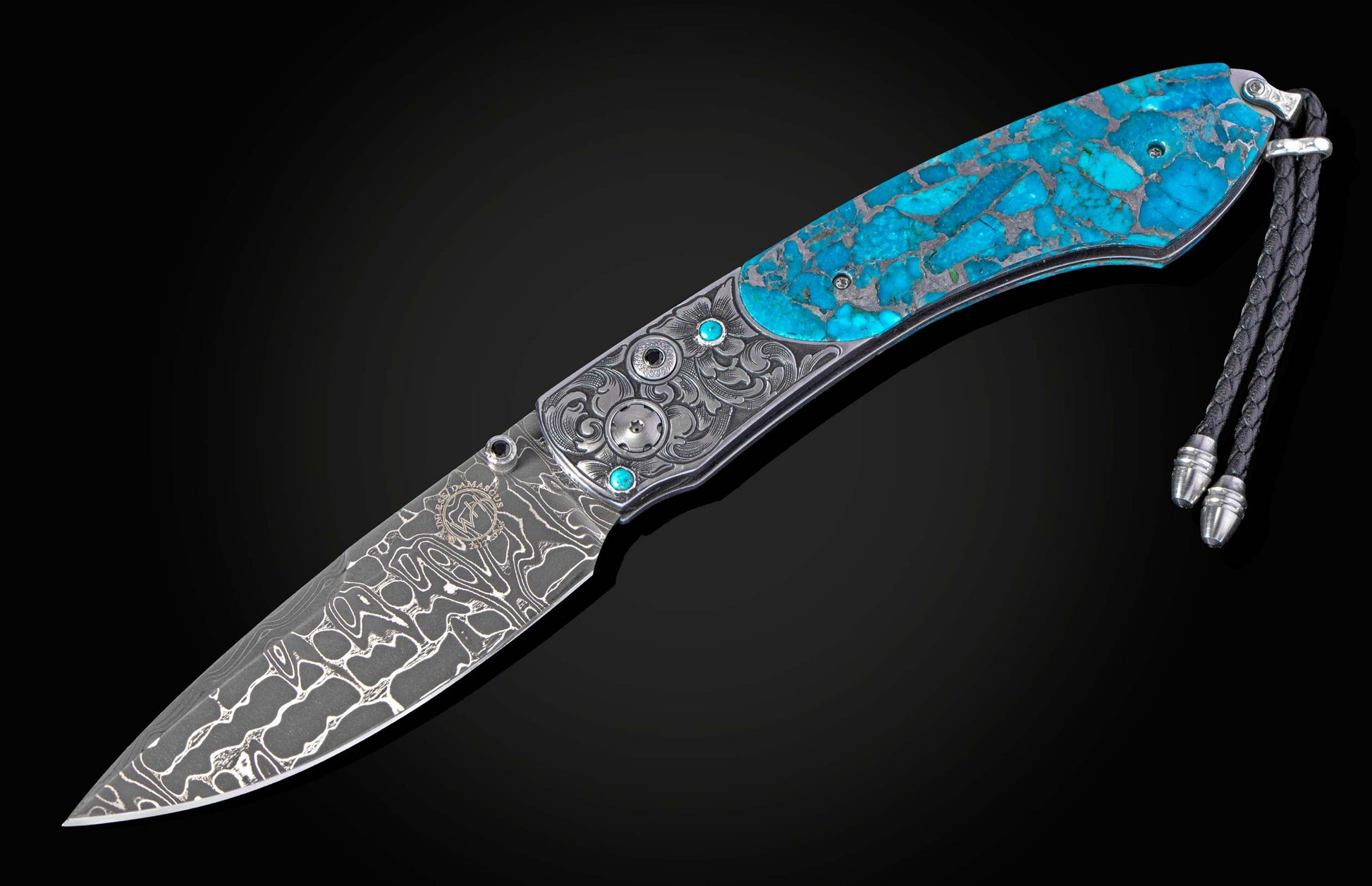 Ornate folding knife with a Damascus blade, an engraved silver handle, and bright blue turquoise stone inlay, featuring a black braided leather lanyard.