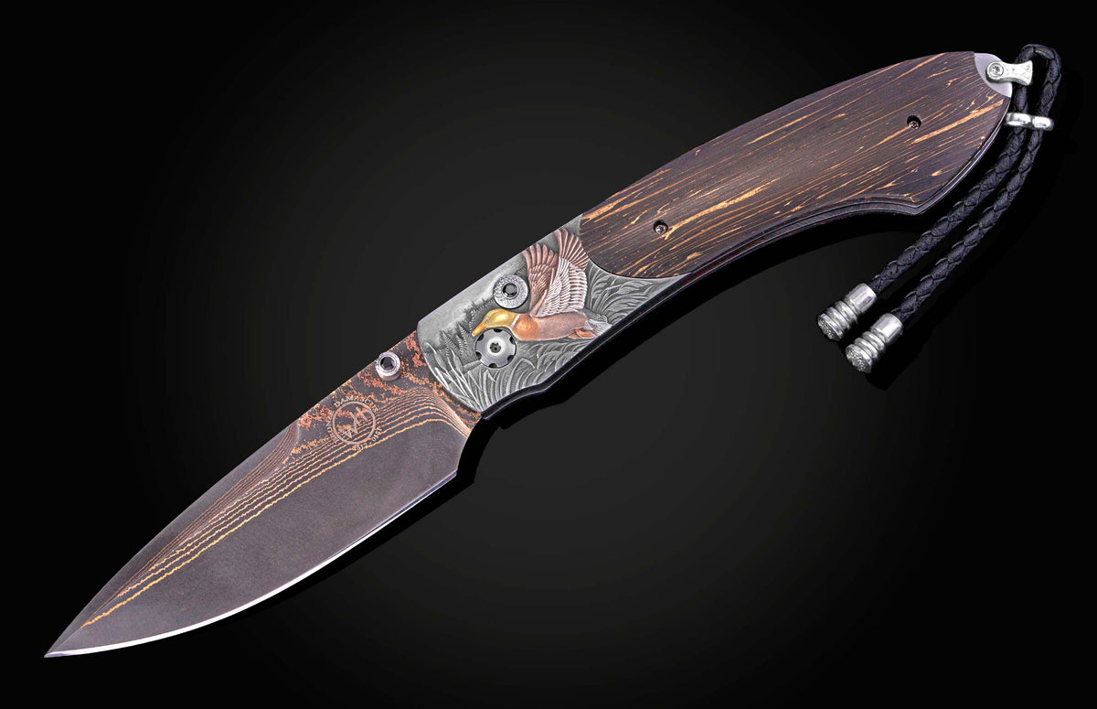 Folding knife with a patterned Damascus blade and a dark wood handle featuring an engraved flying mallard duck, with a black braided lanyard.
