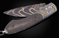 Folding knife with a dark Damascus blade featuring golden-bronze wavy patterns and a handle with intricate metallic inlay.