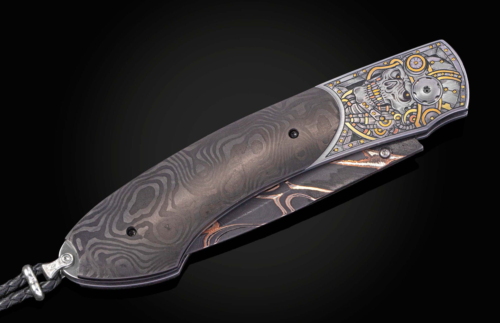 Damascus steel folding knife with an engraved silver and gold skull motif and a braided leather lanyard.