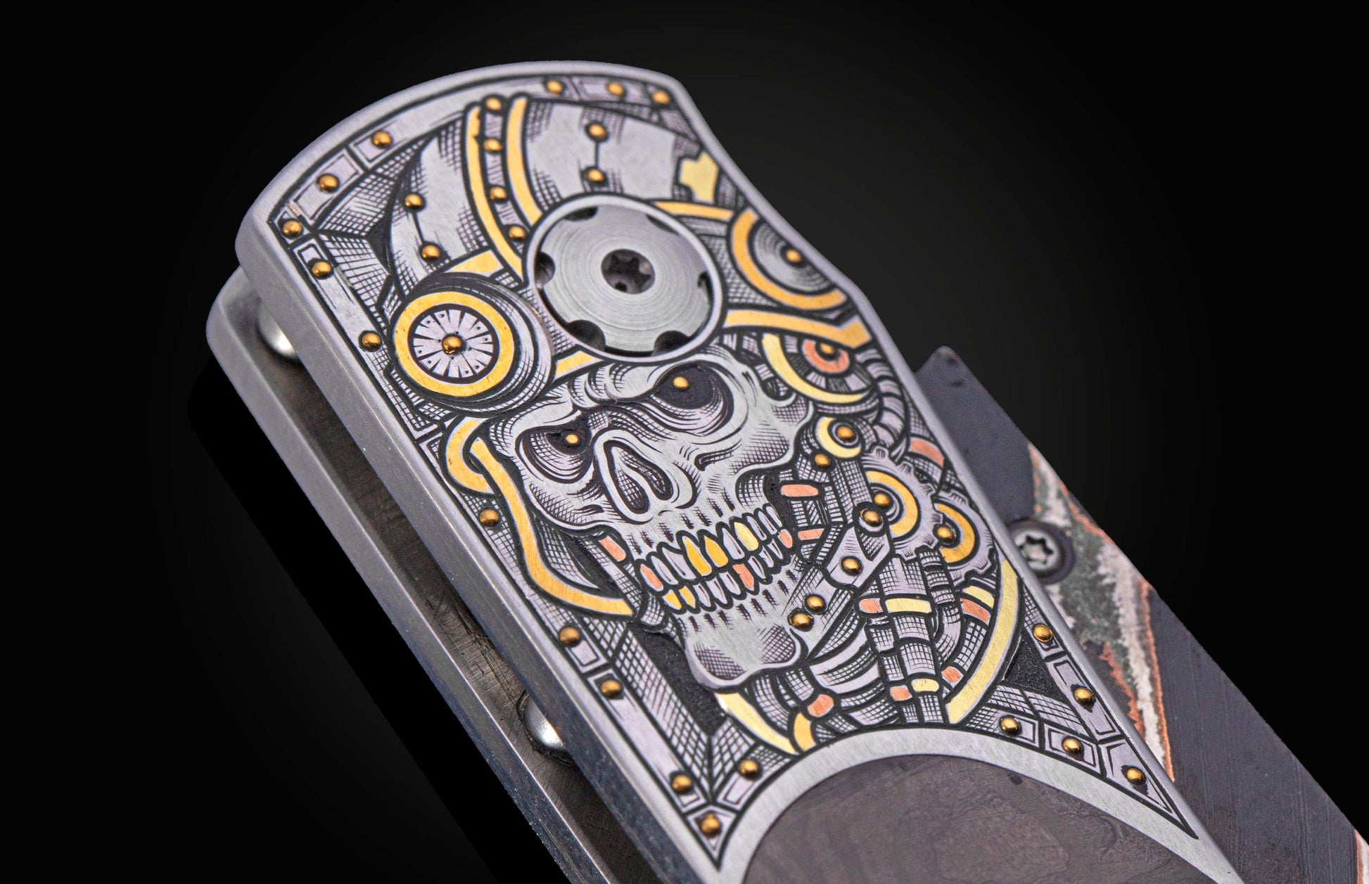Silver engraved folding knife handle with an intricate steampunk-style skull design featuring gold and copper accents, seen close-up.
