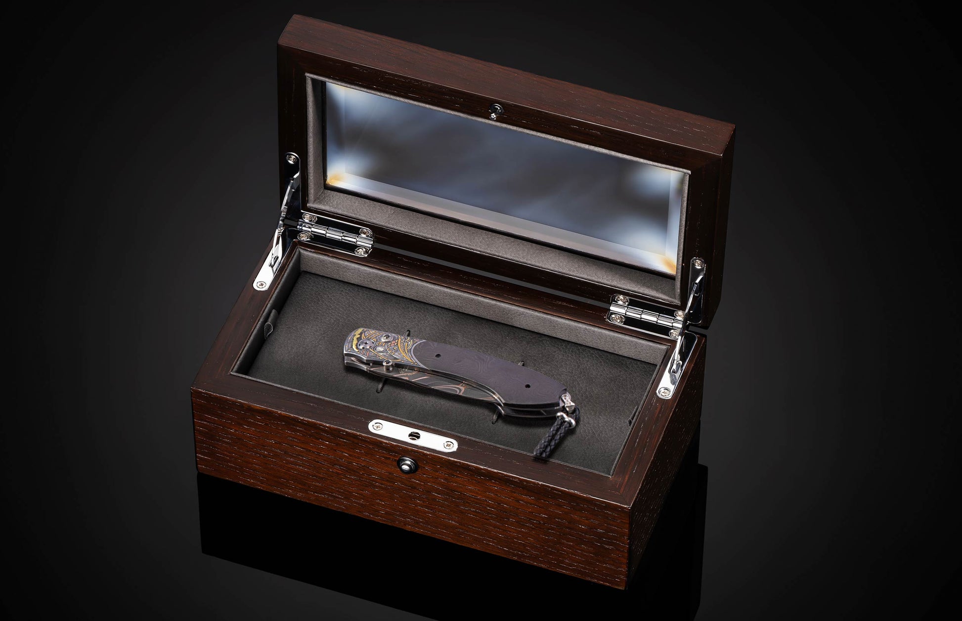 Elaborate folding knife with patterned blade and gold-silver engraved handle, in an open dark wood display box with glass lid.