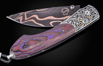Luxury folding knife with bronze damascus blade and purple-red marbled handle, by William Henry, featuring intricate silver filigree and sapphire accents, side view on black background