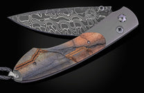 Folding knife with decorative blade and mammoth tooth handle on a black background