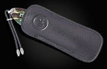 Black leather sheath with embossed logo and braided cord, holding B12 Parallel knife with marbled handle, side view