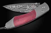 Purple wood handle folding knife with a wavy damascus blade, 'WHH STAINLESS DAMASCUS' etched text, decorative clear studs, and a black braided lanyard.