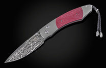 Open folding knife with a patterned stainless Damascus steel blade, rich purple textured handle scales, and a braided black leather lanyard.