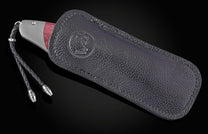 Red wood-handled knife in a black leather sheath with an embossed logo and braided lanyard.