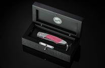 Folding knife with vibrant purple wood handle, Damascus blade, and silver metal accents, displayed in an open black wooden box with a 'WH' logo.