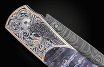 Luxury folding knife with intricate raven engraving and sapphire accents, featuring damascus steel blade and marbled handle, side view close-up