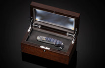 Luxury folding knife with blue marbled handle and intricate silver inlay, by B12, displayed in dark wood presentation box with glass lid, top-down view