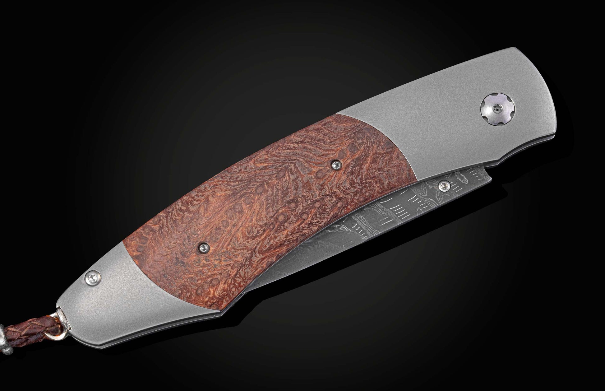 Folding knife with red burl wood and brushed metal handle, Damascus steel blade, and braided leather lanyard.