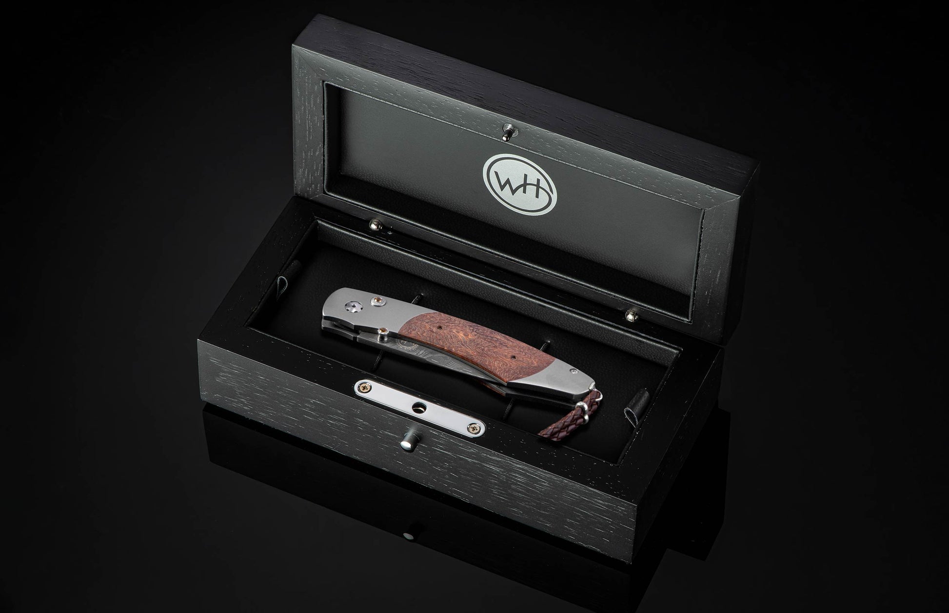 Folding knife with reddish-brown burl wood handle and silver-toned metal, displayed in an open black box with a 'WH' logo.