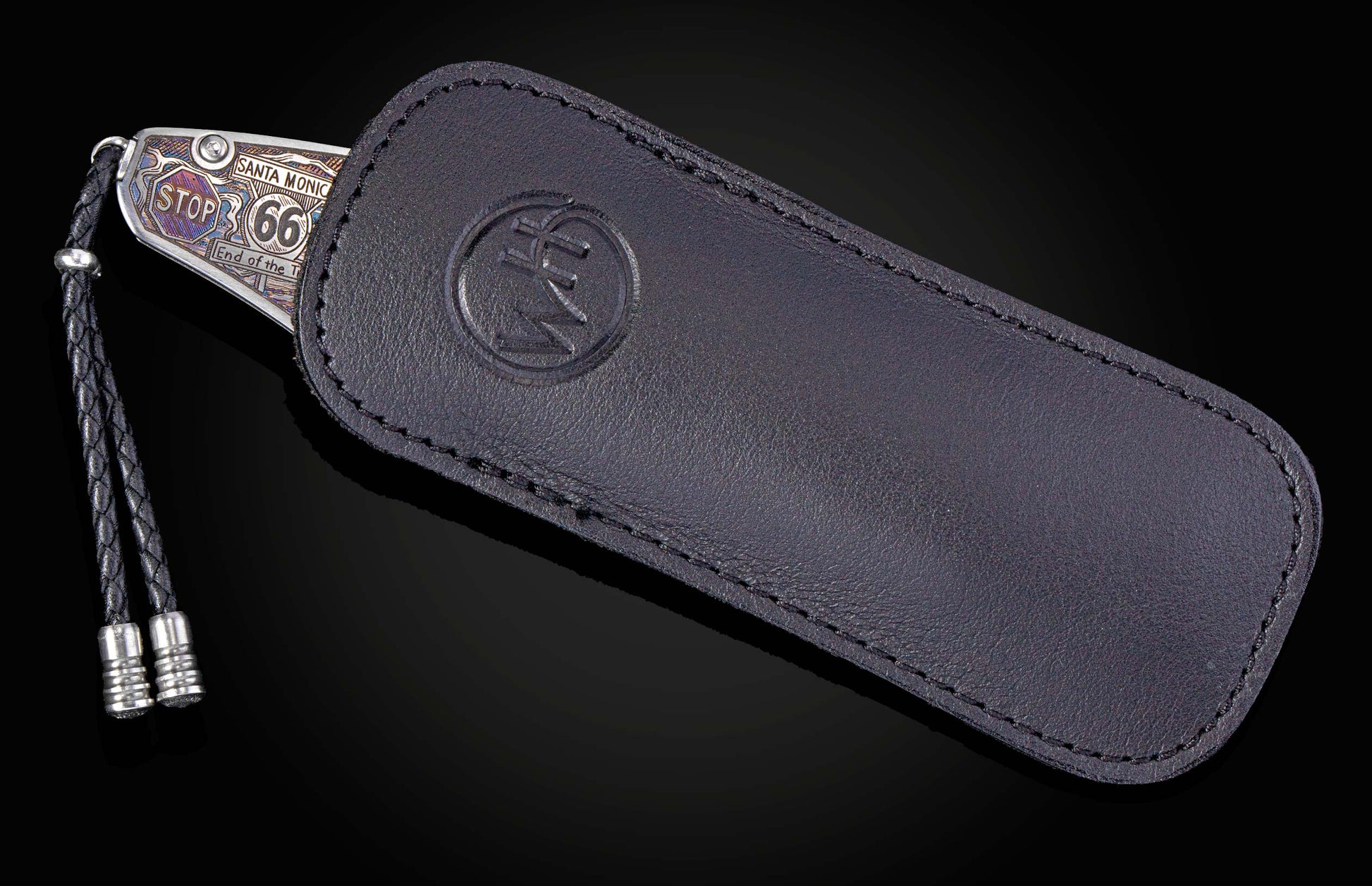 Metallic knife with "Route 66" engraving, braided lanyard, and partially sheathed in black leather featuring a debossed 'WH' logo.