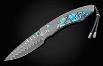 Luxury folding knife with damascus steel blade and turquoise inlay handle, by B12, featuring wave pattern and braided lanyard, side view on black background