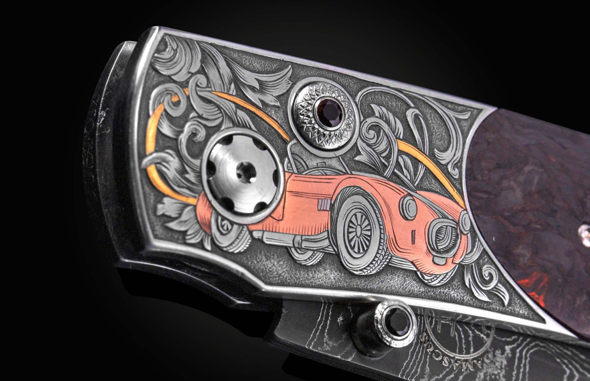 Engraved knife featuring a copper-toned Shelby Cobra car design, intricate silver scrollwork, and a dark gemstone on a dark handle.