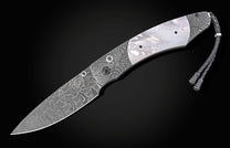 Damascus steel knife with silver wave pattern and mother-of-pearl inlay, featuring braided cord lanyard, side view on black background