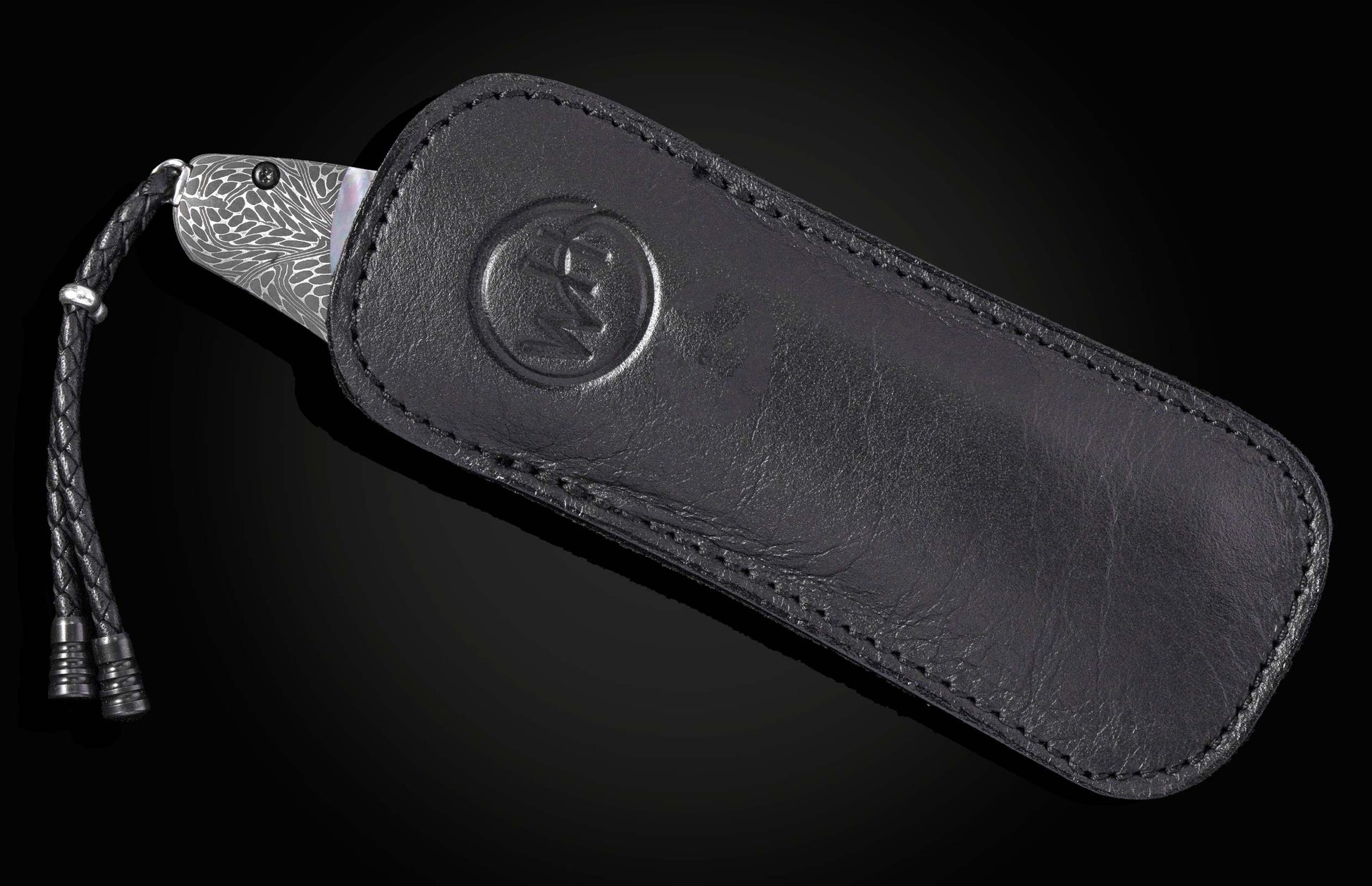 Silver patterned blade knife in black leather sheath with embossed logo and braided lanyard, side view
