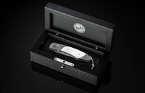 Silver folding knife with damascus steel handle and mother-of-pearl inlay by William Henry, displayed in black presentation box, top-down view
