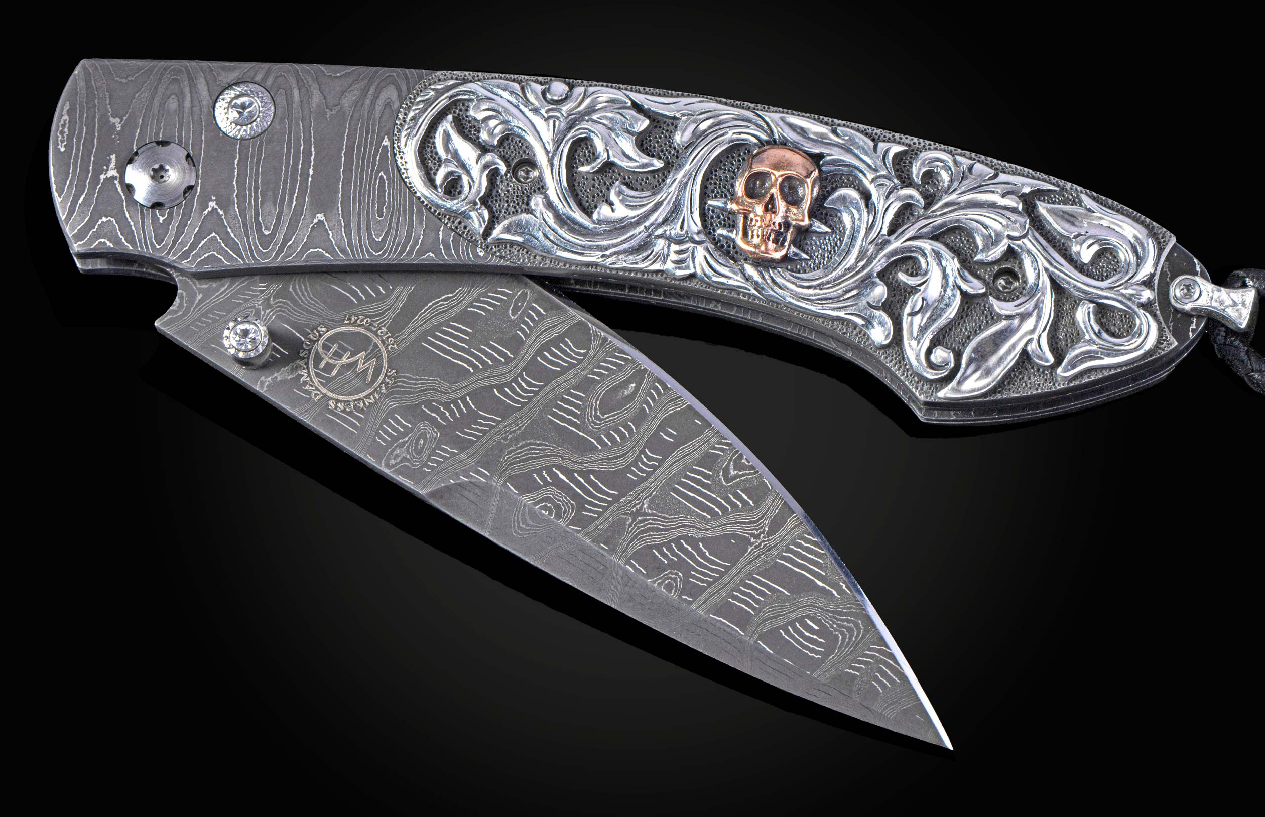 Partially open Damascus steel folding knife with ornate silver handle engraving featuring a rose gold skull.