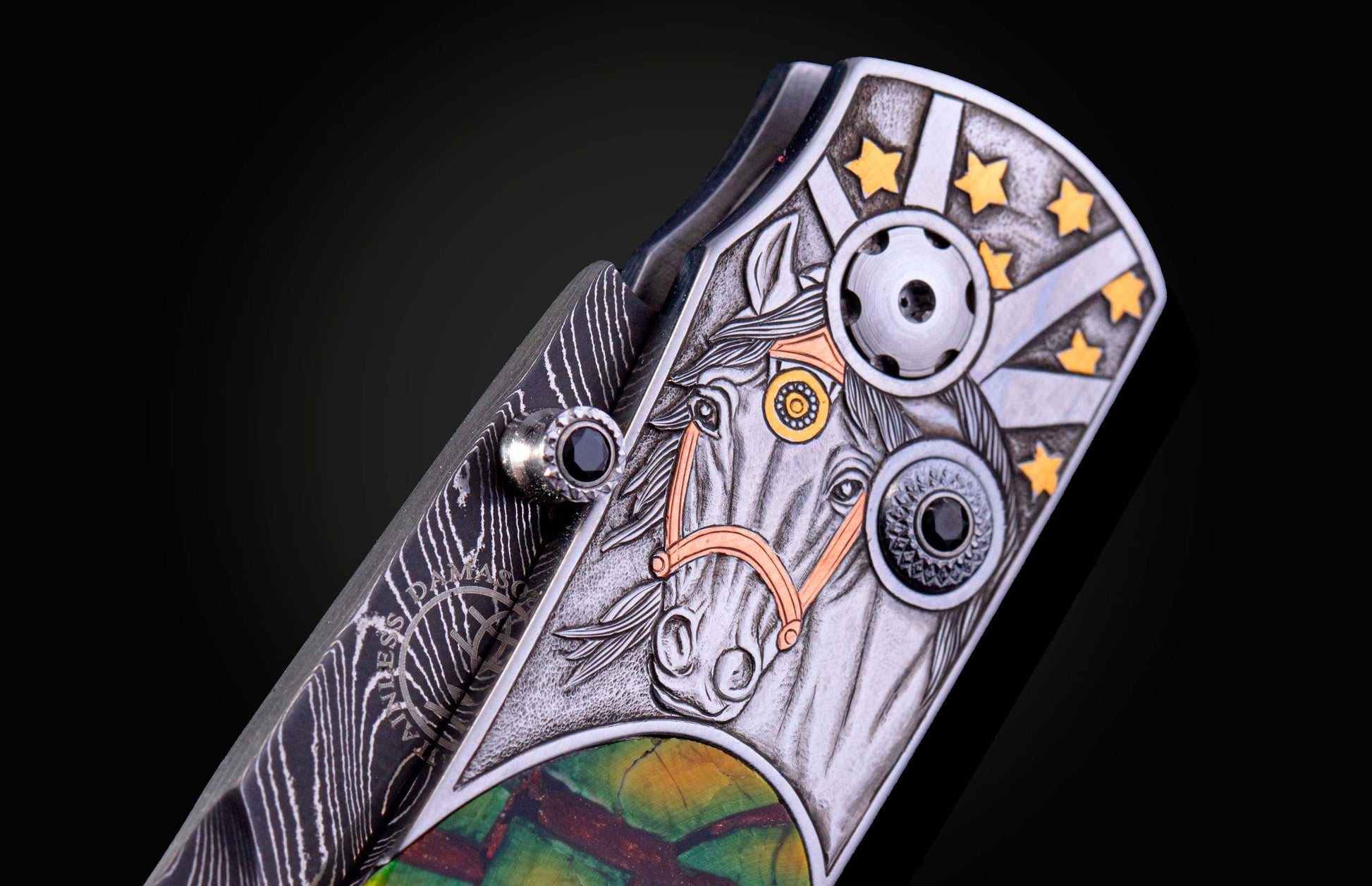 Ornate knife handle with an engraved silver horse head, gold stars, Damascus steel, a black gemstone, and colorful inlay.