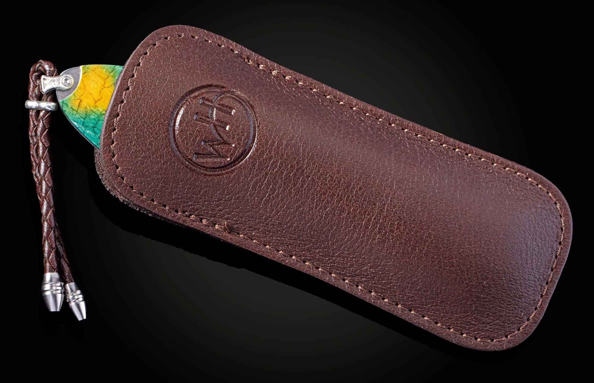 Knife with a yellow and green marbled handle, partially visible in a brown leather sheath with an embossed logo and a braided lanyard.