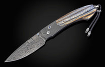 Damascus steel folding knife with wavy pattern blade, layered blue-orange handle scales, blue inlays, and black braided leather lanyard.