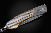 Closed knife with patterned Damascus steel, a rustic multi-toned handle, and braided black leather lanyard.