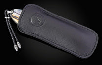 Knife with an iridescent handle and braided lanyard, partially sheathed in black leather with a debossed logo, on a reflective surface.