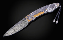 Ornate folding knife with a Damascus blade and an engraved handle featuring wildlife scenes with gold accents.