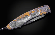Decorative folding knife with silver and gold engravings of a deer, wolves, and a bird in a winter forest.