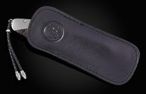 Dark leather-sheathed knife with an embossed logo, revealing a metallic grip and textured fossil handle, plus a braided lanyard.