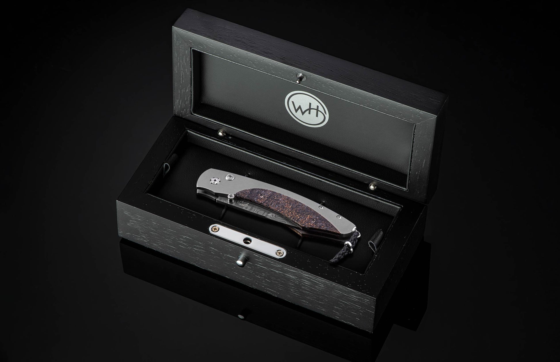 Folding knife with grey metal and textured brown handle, Damascus blade, in an open black display box.