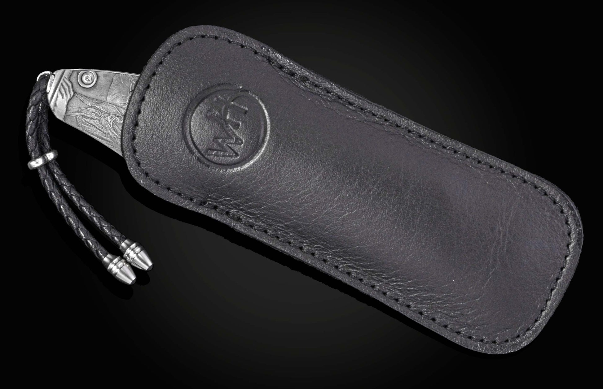 A silver-toned knife with an intricate pattern, partially sheathed in a black leather pouch with an embossed logo and a braided leather lanyard.