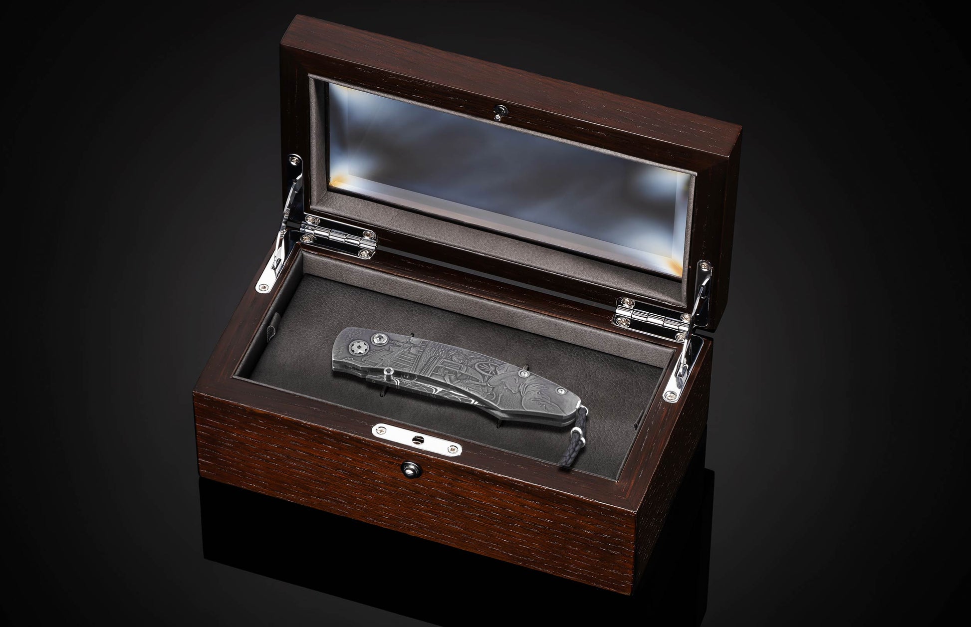 Engraved metal knife with a Western scene in an open dark wood display box with glass lid.