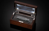 Engraved metal knife with a Western scene in an open dark wood display box with glass lid.