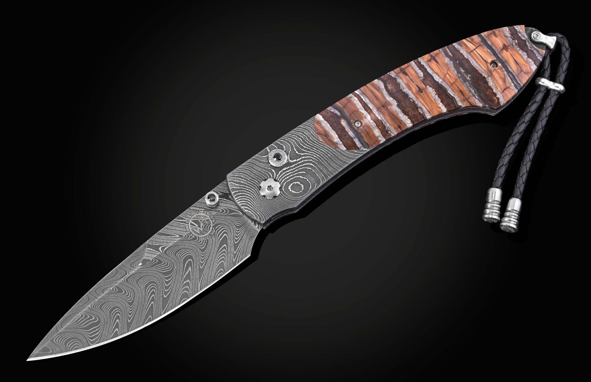 Knife with a wavy Damascus steel blade, striped brown and white handle with silver hardware, and a black braided lanyard.