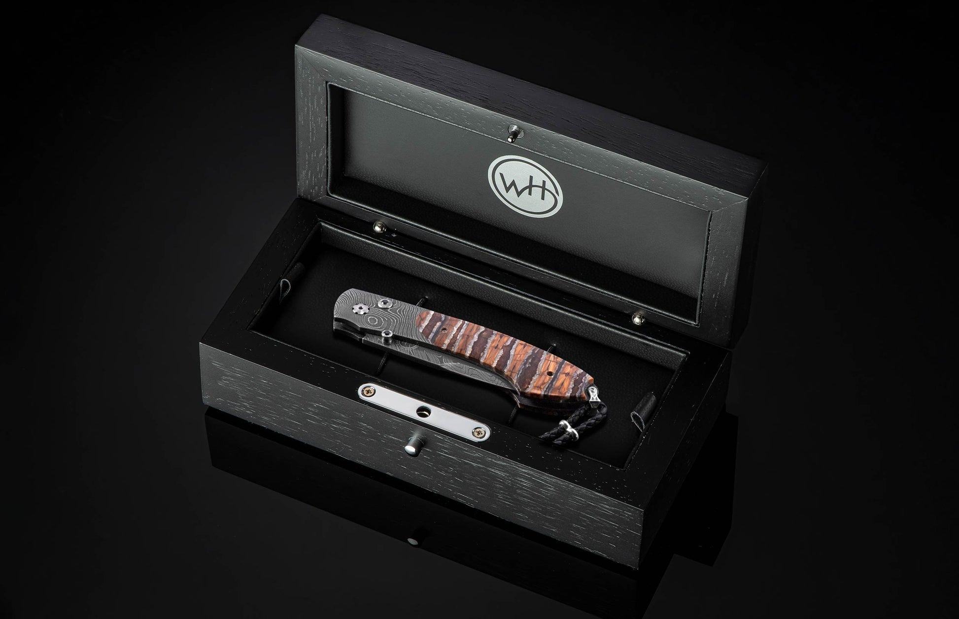 Folding knife with a patterned Damascus blade and striped natural handle, presented in an open black wooden display box.