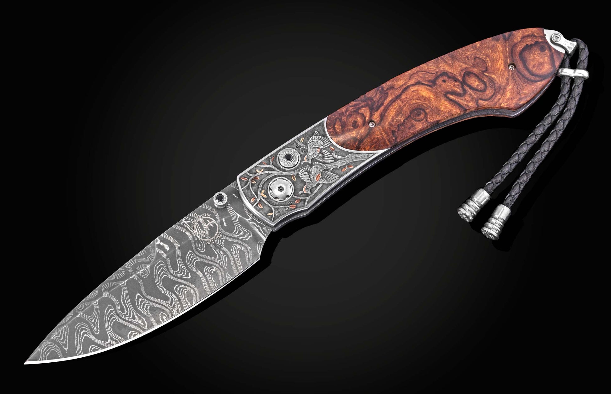 Damascus steel knife with intricate quail engraving and burl wood handle by B12, featuring silver hardware and braided lanyard, side view on black background