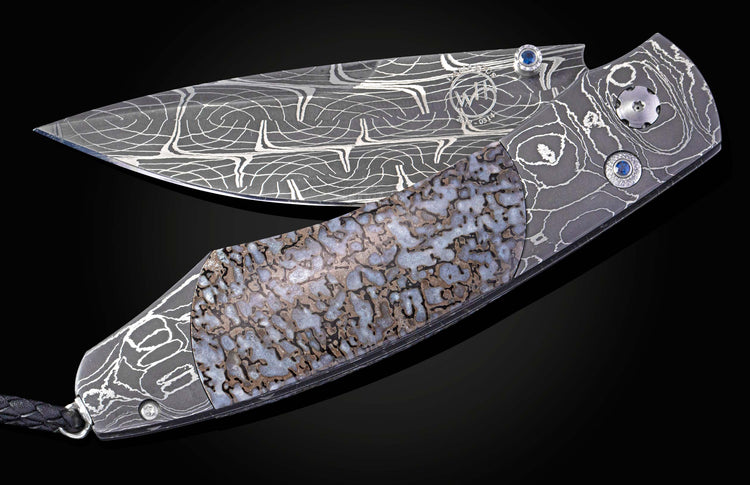 Partially open custom folder knife featuring a patterned Damascus blade, fossilized handle inlay, and blue gemstone accents.