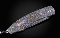 Folding knife with a dark damascus steel handle, a blue-brown fossilized inlay, and a braided lanyard.