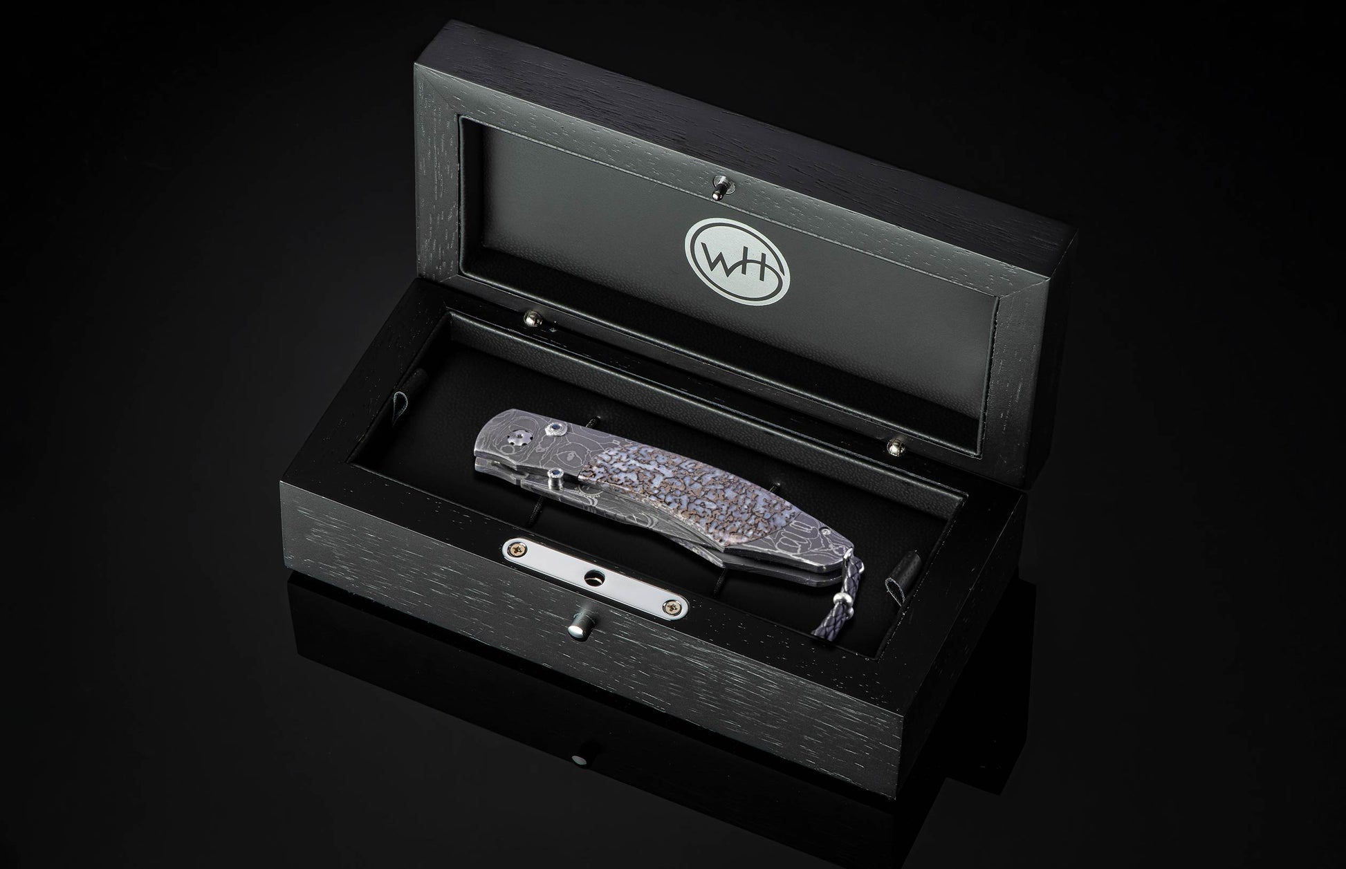 Folding knife with a damascene blade and intricate patterned handle, displayed in an open dark wood presentation box with a lanyard.