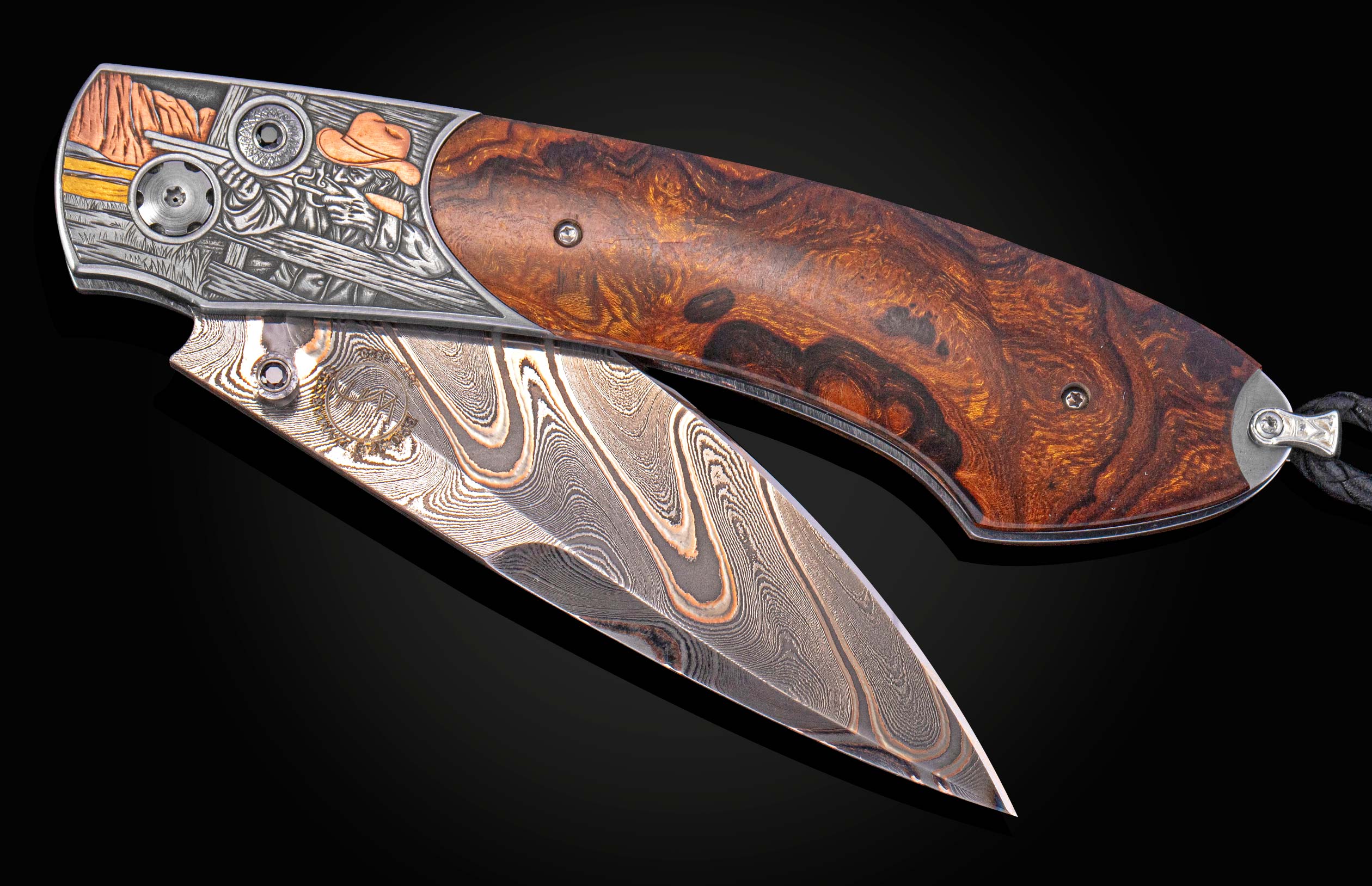 Custom folding knife with a Damascus steel blade, engraved metal frame depicting a Western scene, burl wood handle, and black leather lanyard.