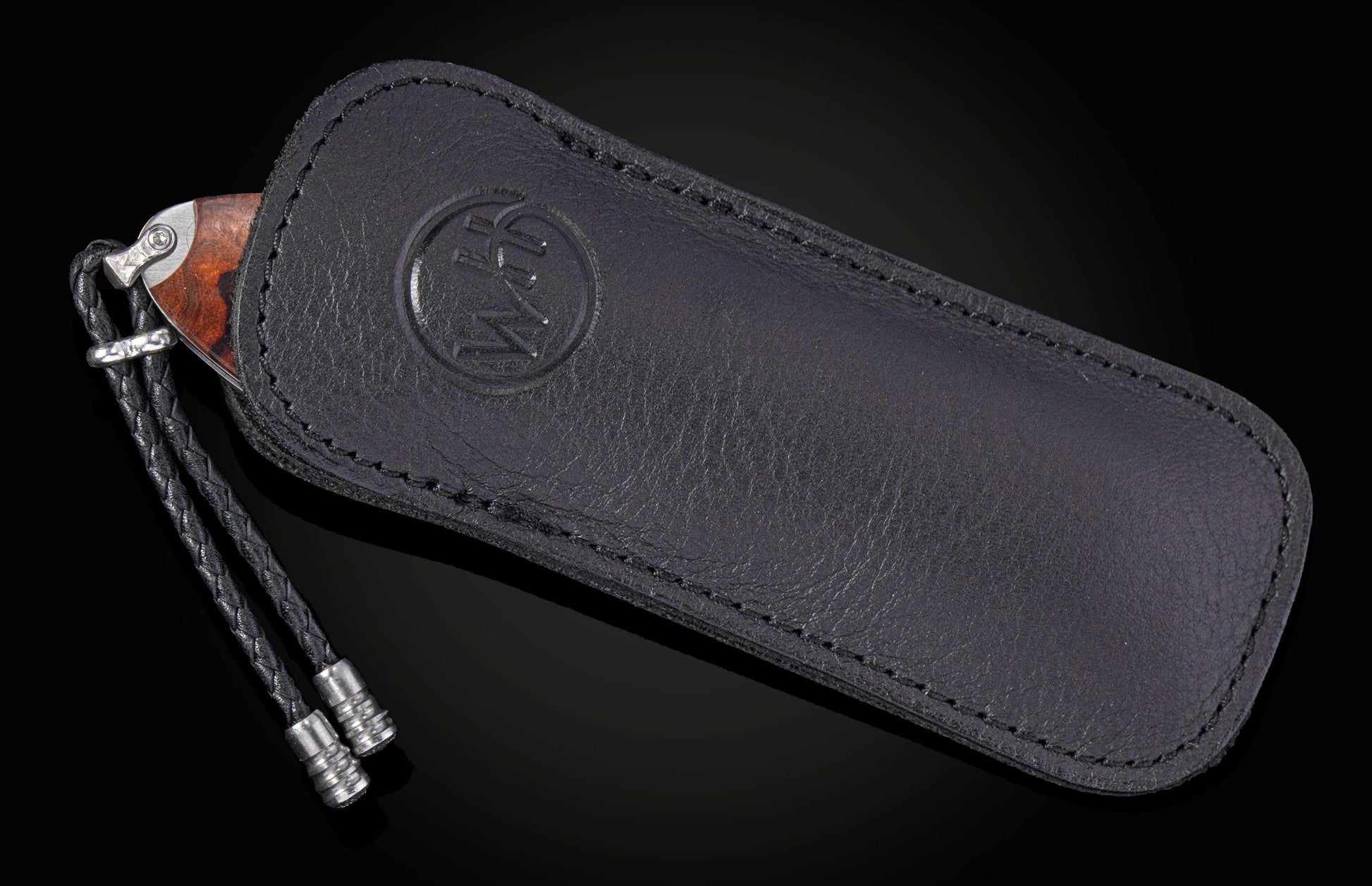 Dark wood handled knife with a black braided leather lanyard, partially in a black leather sheath featuring an embossed WH logo.